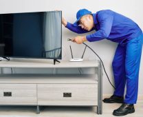 Serious young Vietnamese repairman installing tv set in apartment of customer